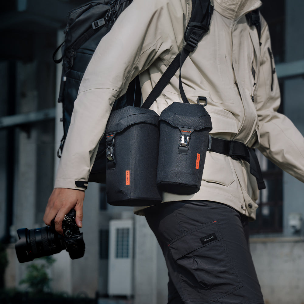 A photographer keeps two lens cases on his belt for fast lens swaps while shooting on the go in the city.